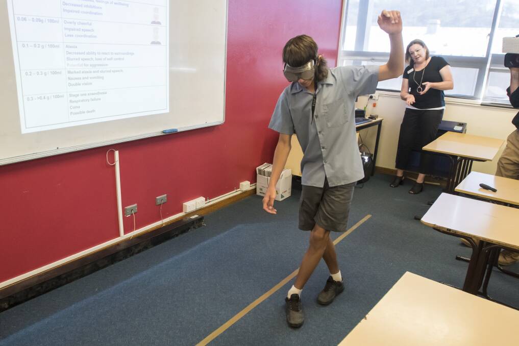 INFLUENCE: Oxley High School Year 9 students try to walk a straight line in the 'alcohol vision' goggles, while Life Education's Angela Green looks on. Photo: Peter Hardin 200318PHA123