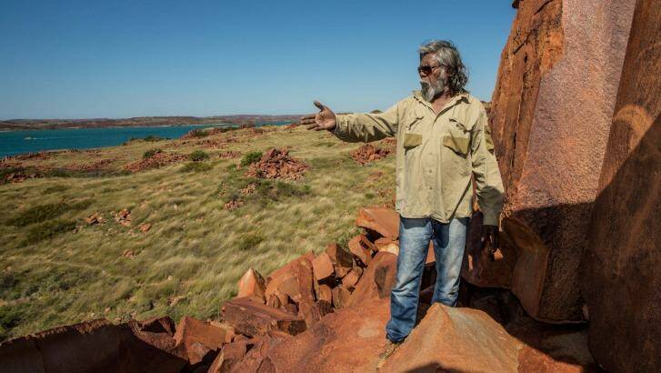 The rock art on the Burrup represent more than 30,000 years of continuous living culture. Senior cultural ranger at Murujuga National Park, Jakari Togo, looks out to sea next to rock carvings on the Burrup Peninsula. Photo: Australian Geographic