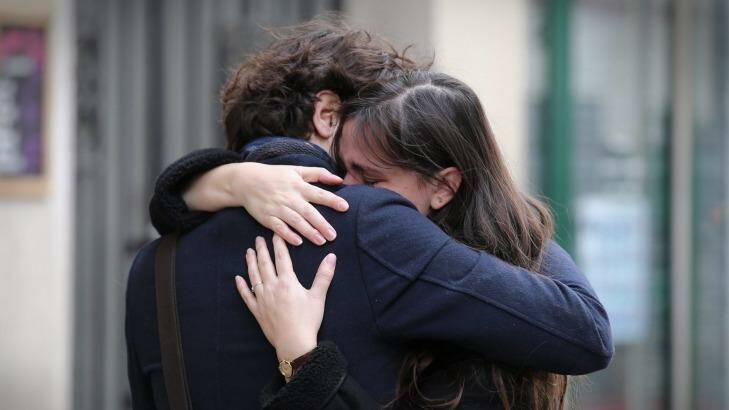 A couple embrace after laying flowers at the La Belle Equipe cafe on Saturday. Photo: Andrew Meares