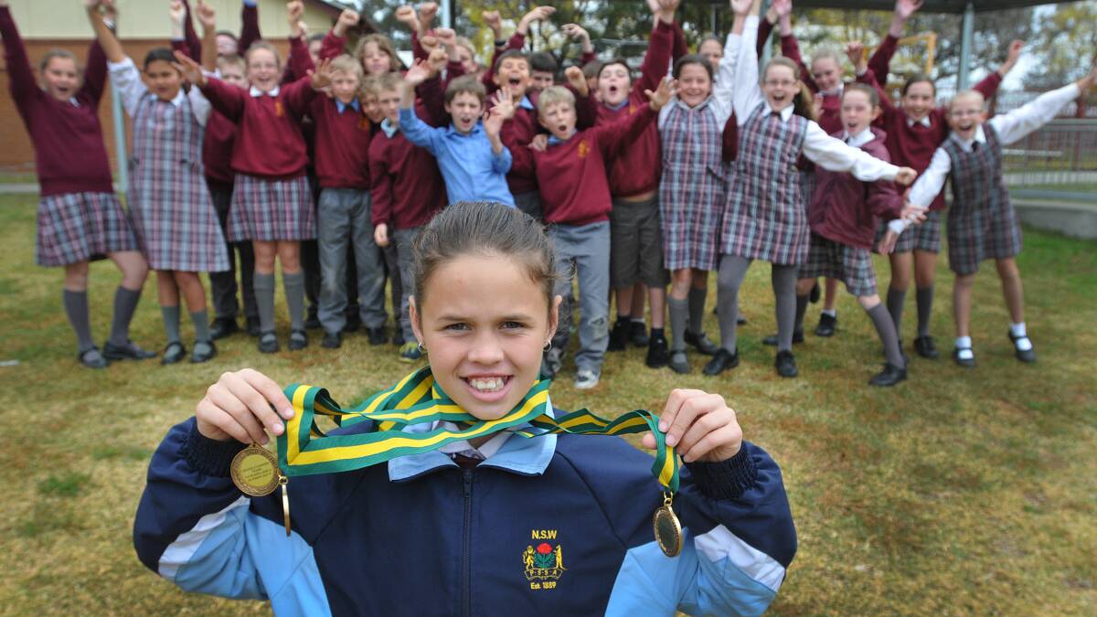 New Australian U10 Cross Country champion Lacie Quigley with her brace of national medals, and her class 5A supporters in the background.  Photo: Geoff O’Neill 270814GOA01