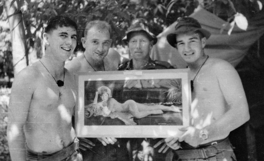 An informal group portrait of four members of 6th Battalion, The Royal Australian Regiment (6RAR) holding a framed pin-up girl portrait. Identified is 2nd Lieutenant Gordon Cameron Sharp, left. The others are unidentified. Photo: P09388.003