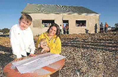 Plan of action: Camp Quality’s Christine Gardner and Ethan Wighton, with Amber the cattle dog pup, go over plans for the completion of the Wightons’ shed, as tradesmen check out what has to be done. Photo: Barry Smith