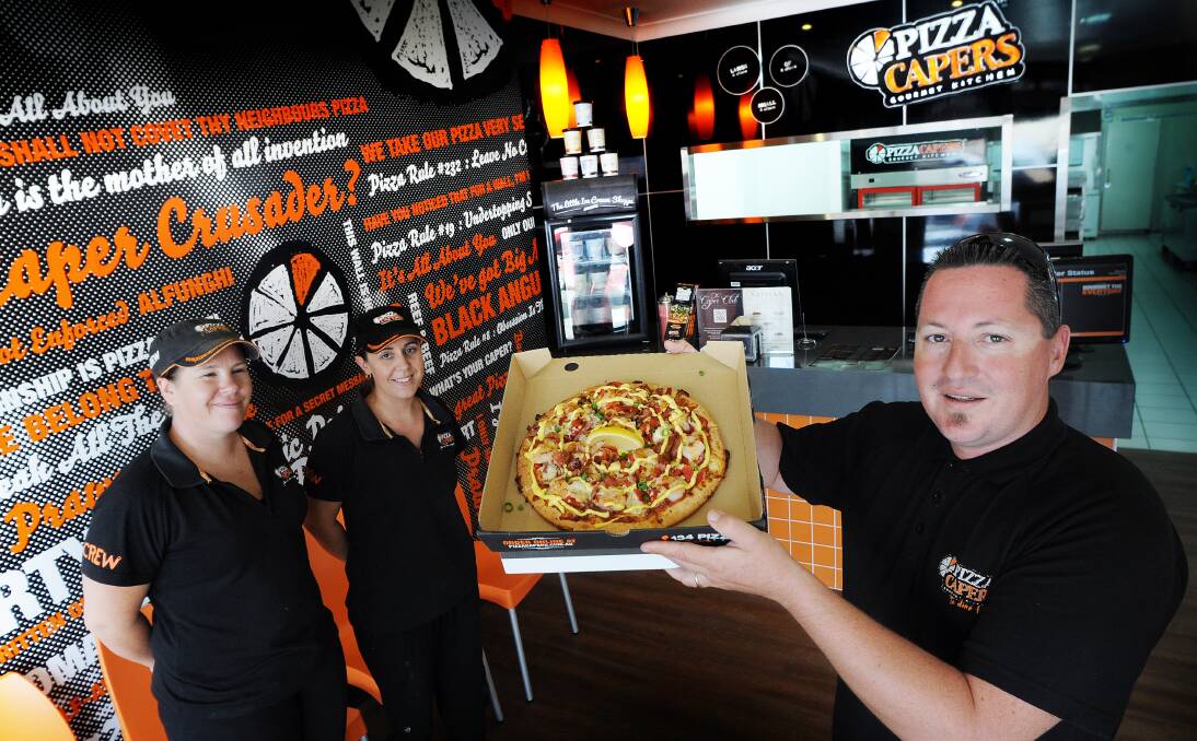 TOP THAT: Tamworth Pizza Capers franchisee Trent Green shows off one of the store’s signature reef and beef pizzas on its first day of business on Monday, while manager Rebecca Meloni and co-franchisee Renee Green look on. Photo: Gareth Gardner 231213GGA10