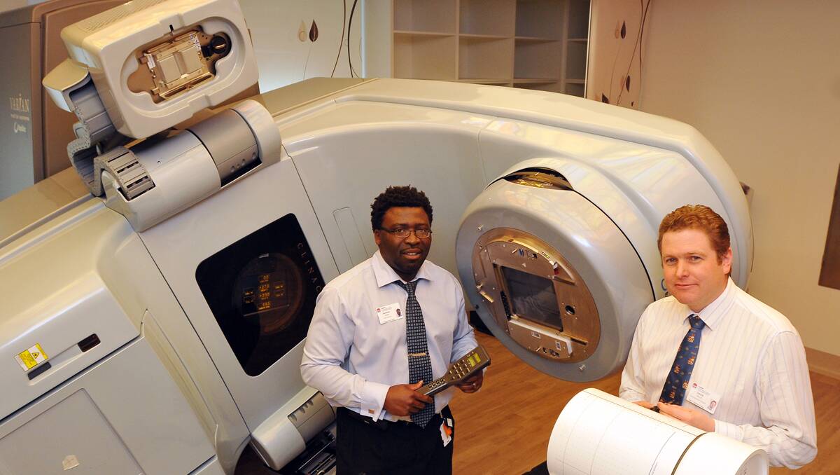 NEARLY HERE: From left, North West Cancer Centre chief physicist Jackson Zifodya and chief radiation therapist David Willis with the linear accelerator. Photo: Geoff O’Neill 180713GOC01