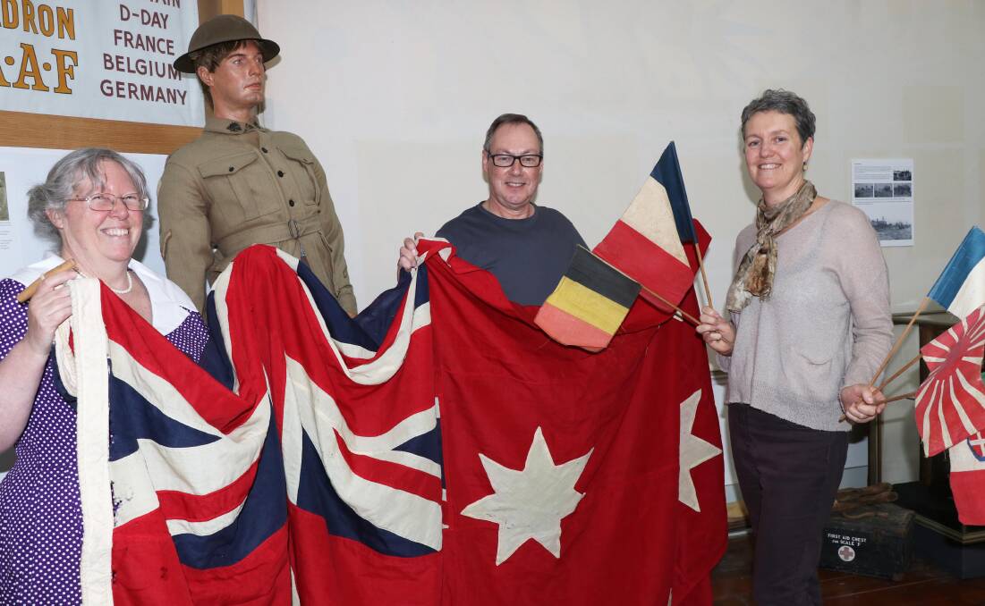 Remembrance: Armidale Folk Museum staff Bronwyn Clarke, Ivan Thornton and Hayley Ward hold an Australian Red Ensign and allied flags used by local citizens to celebrate the end of World War I. Photo: Supplied.