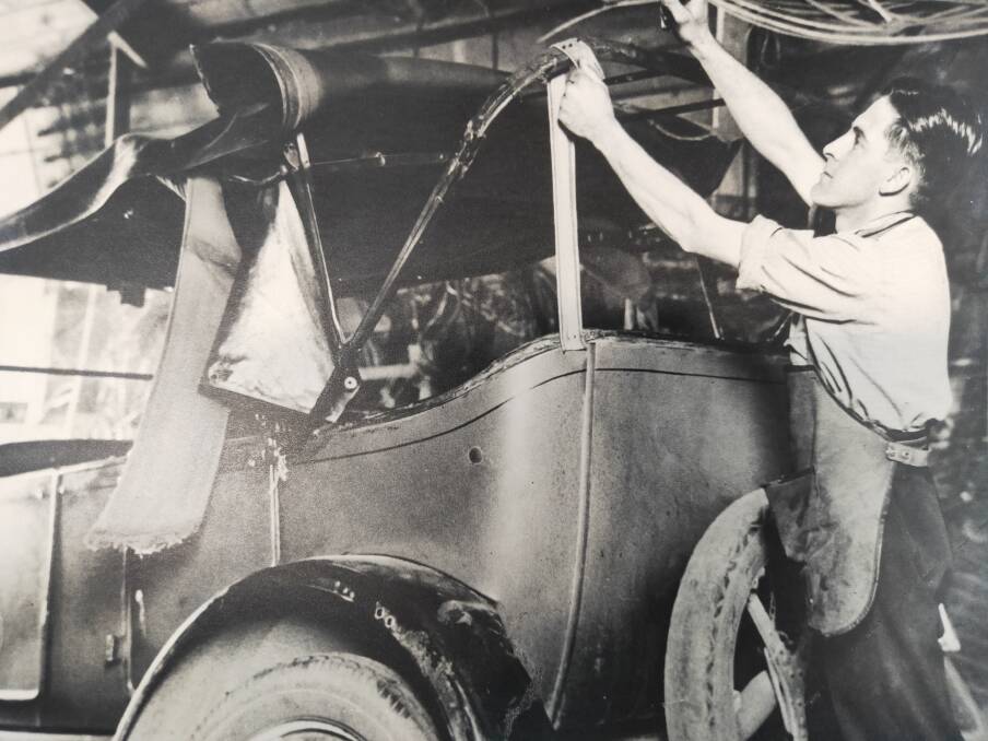 BEGINNINGS: Neville Woodley at work fixing the trimmings of a car in the 1920s.