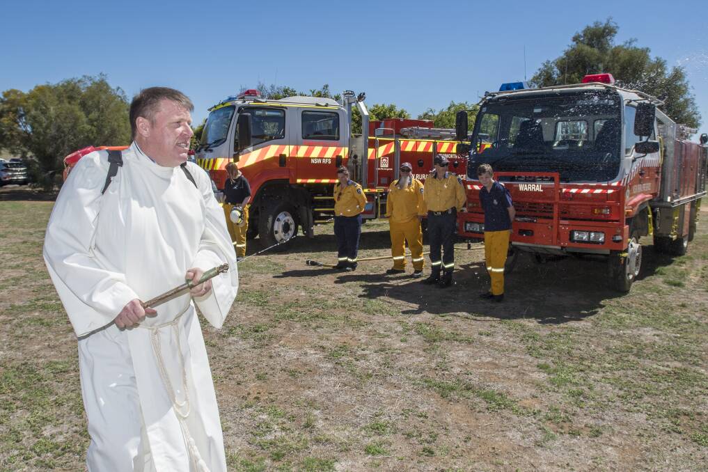 SAFETY, THANKS: Reverend Simon Hansford sprays the RFS vehicles and volunteers during the blessing on Sunday. Photo: Peter Hardin 160918PHA012