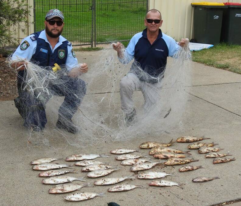 Netted: A police officer and a DPI Fisheries officer hold up the illegal mesh net with the 29 that two people were allegedly caught with at Keepit Dam.