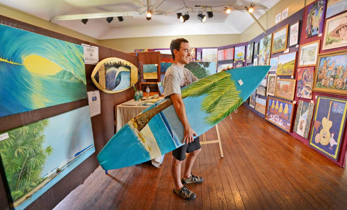 SURF'S UP: Scott Denholm, former artist in residence with his artworks and painted surfboard at the 2015 exhibition. Photo: Barry Smith 