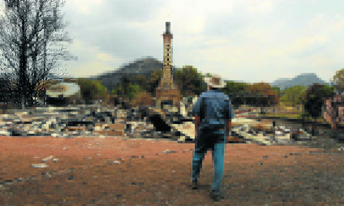 INQUIRY UNDER WAY: A Coonabarabran farmer surveys the remains of his burnt-out home after a 
devastating bushfire swept through the district in January last year. Photo: Jacky Ghossein