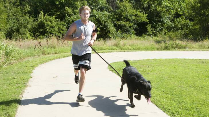 A young man runs with his large black lab. Generic.